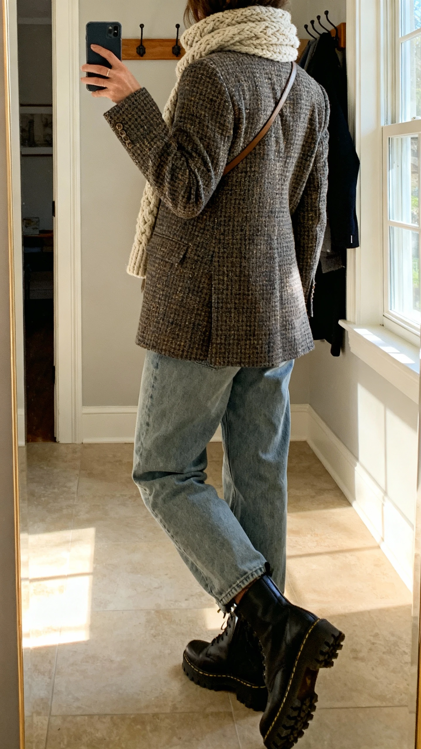 iPhone back-view selfie of a woman wearing a tweed blazer, relaxed dad jeans, chunky knit scarf, lug-sole boots, and a crossbody; face not visible, entryway mirror with coat rack, afternoon window light, natural iPhone photo quality.