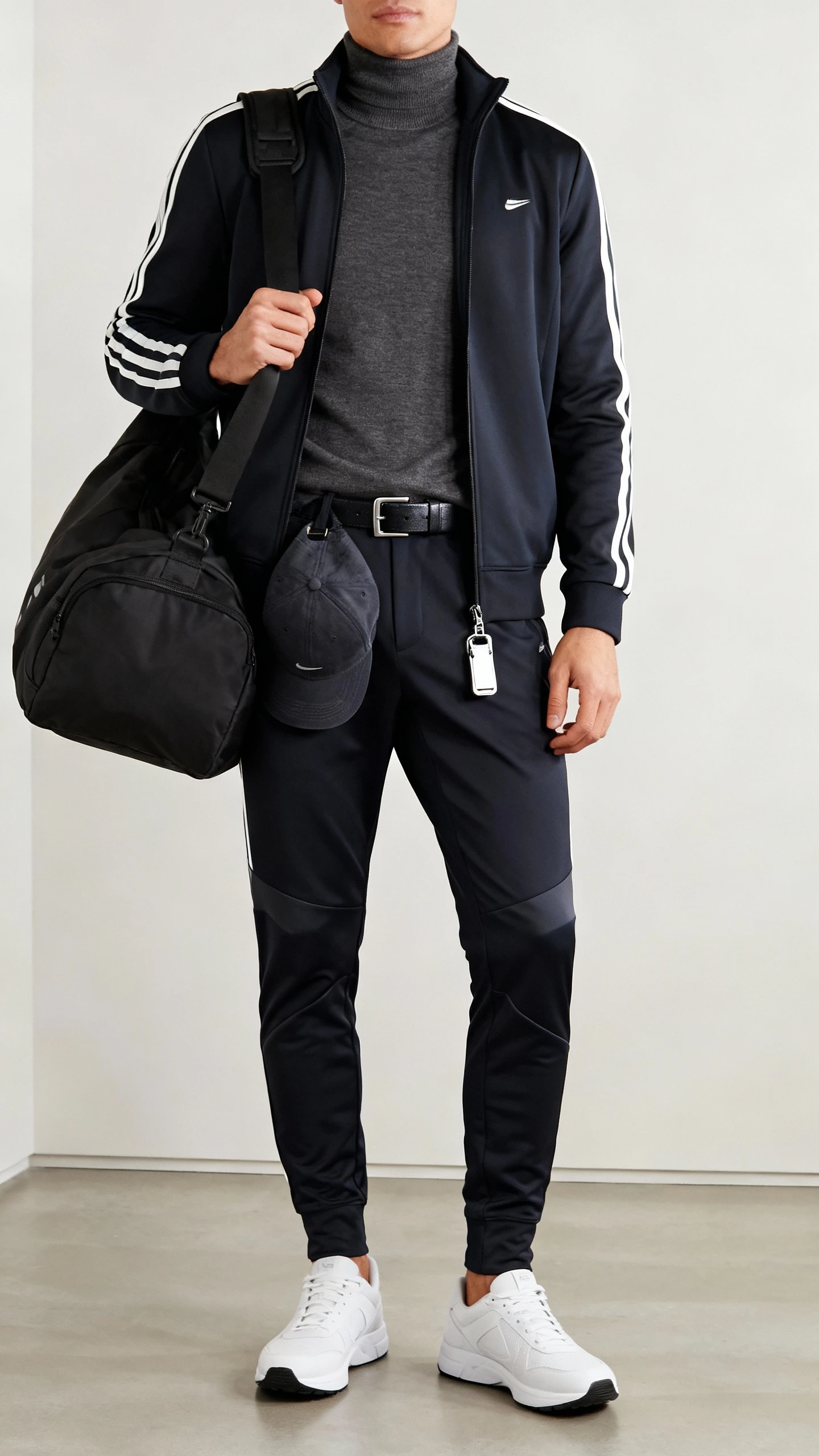 iPhone hallway mirror selfie of a man in sporty luxe: sleek track jacket layered over a merino turtleneck, tapered tech joggers, clean white trainers, and a cap clipped to a belt loop, gym bag on shoulder, bright indoor lighting, face not visible, natural iPhone photo quality.