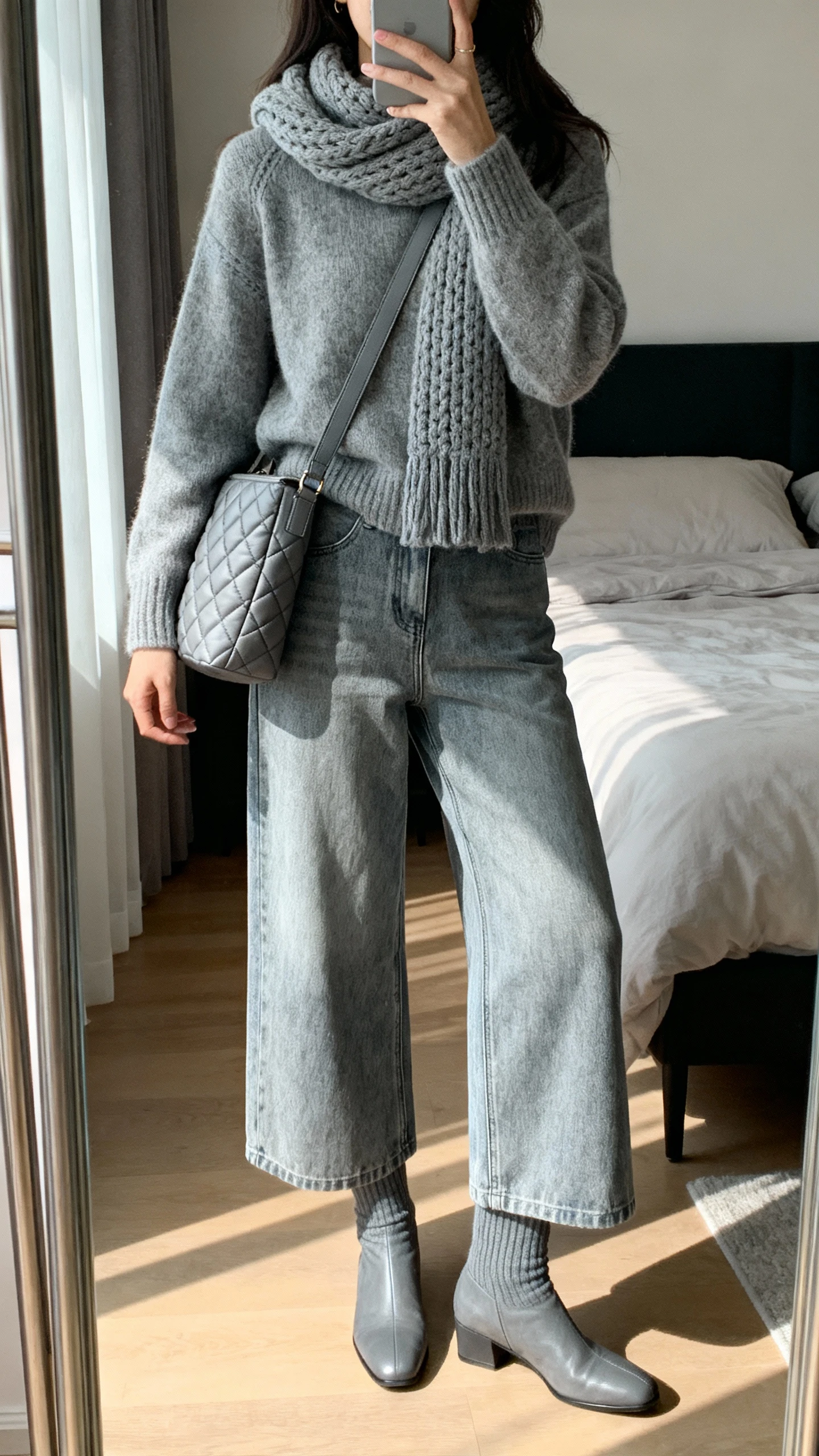 iPhone mirror selfie of a woman wearing a monochrome knit set (matching sweater and knit scarf) with wide-leg jeans in the same tone, sleek sock boots, and a quilted shoulder bag, face not visible, bedroom mirror, diffuse afternoon light, iPhone photo quality.