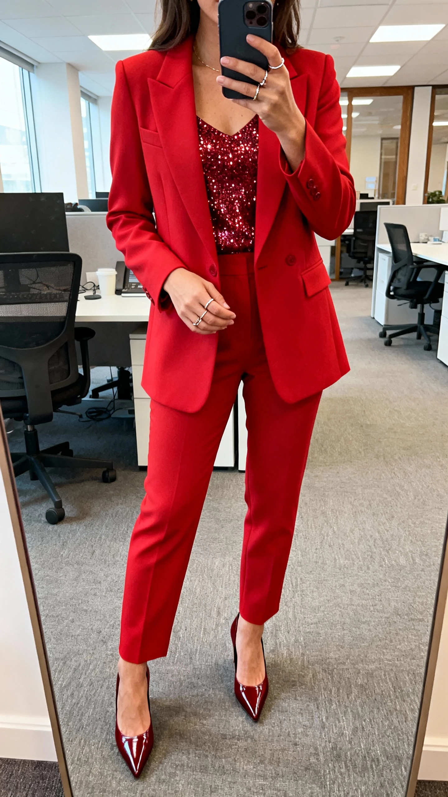 iPhone office mirror selfie of a woman in a statement red suit with a sparkly top underneath, pointed pumps, dainty rings, face not visible, cropped at shoulders, bright office lighting, natural iPhone photo.
