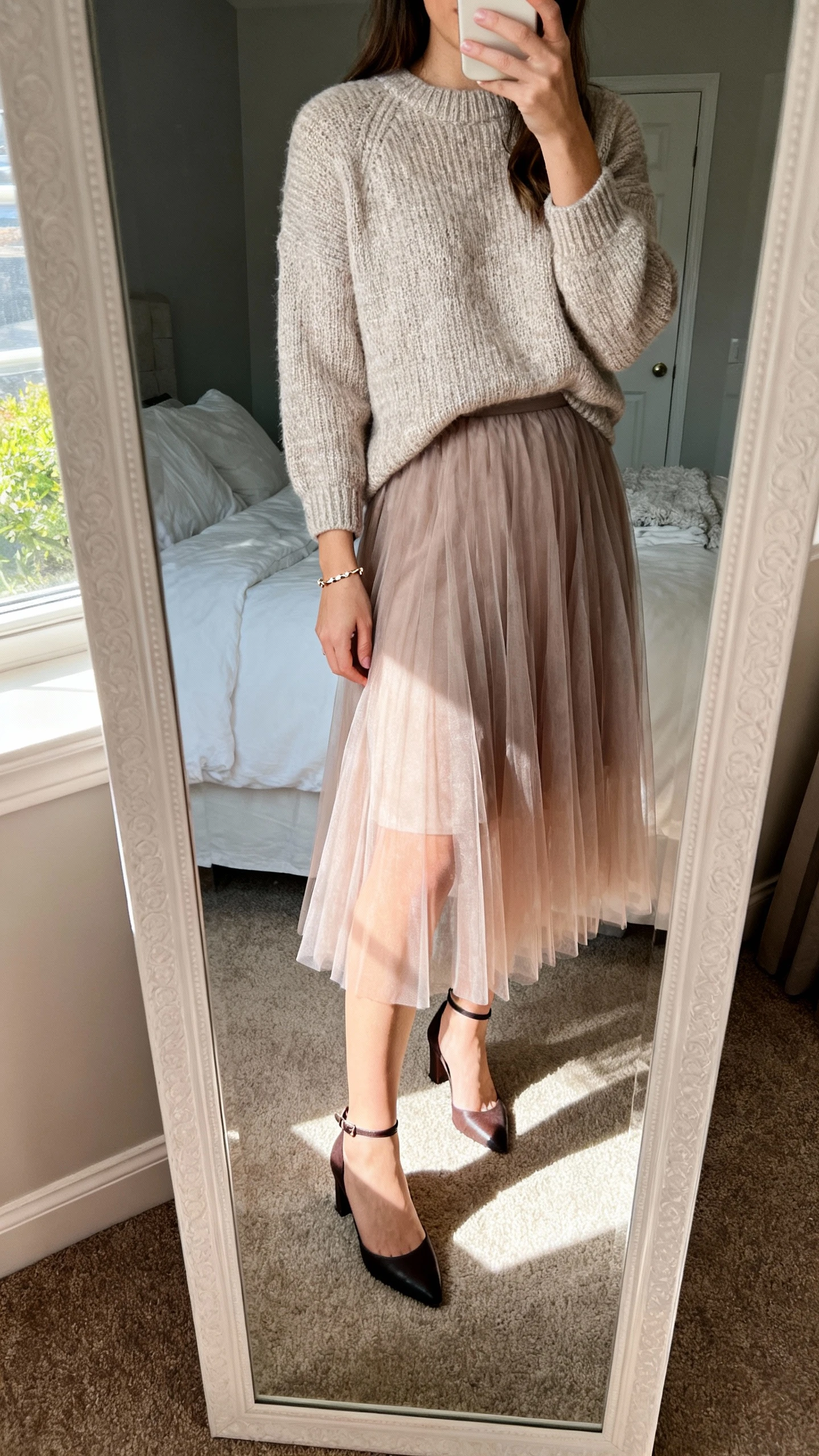 iPhone mirror selfie of a woman in a flirty tulle skirt paired with a cozy cashmere sweater, ankle-strap heels, and a dainty bracelet, face not visible, cropped at shoulders, bedroom mirror, afternoon window light, iPhone photo quality.