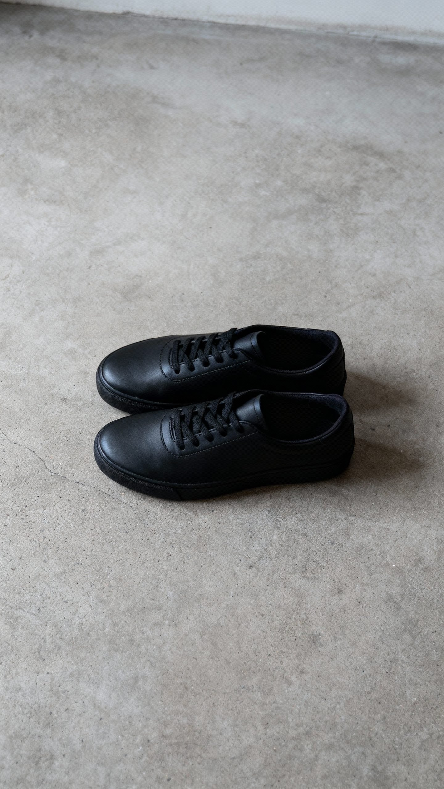 black minimalist sneakers on concrete floor, top-down, diffused light