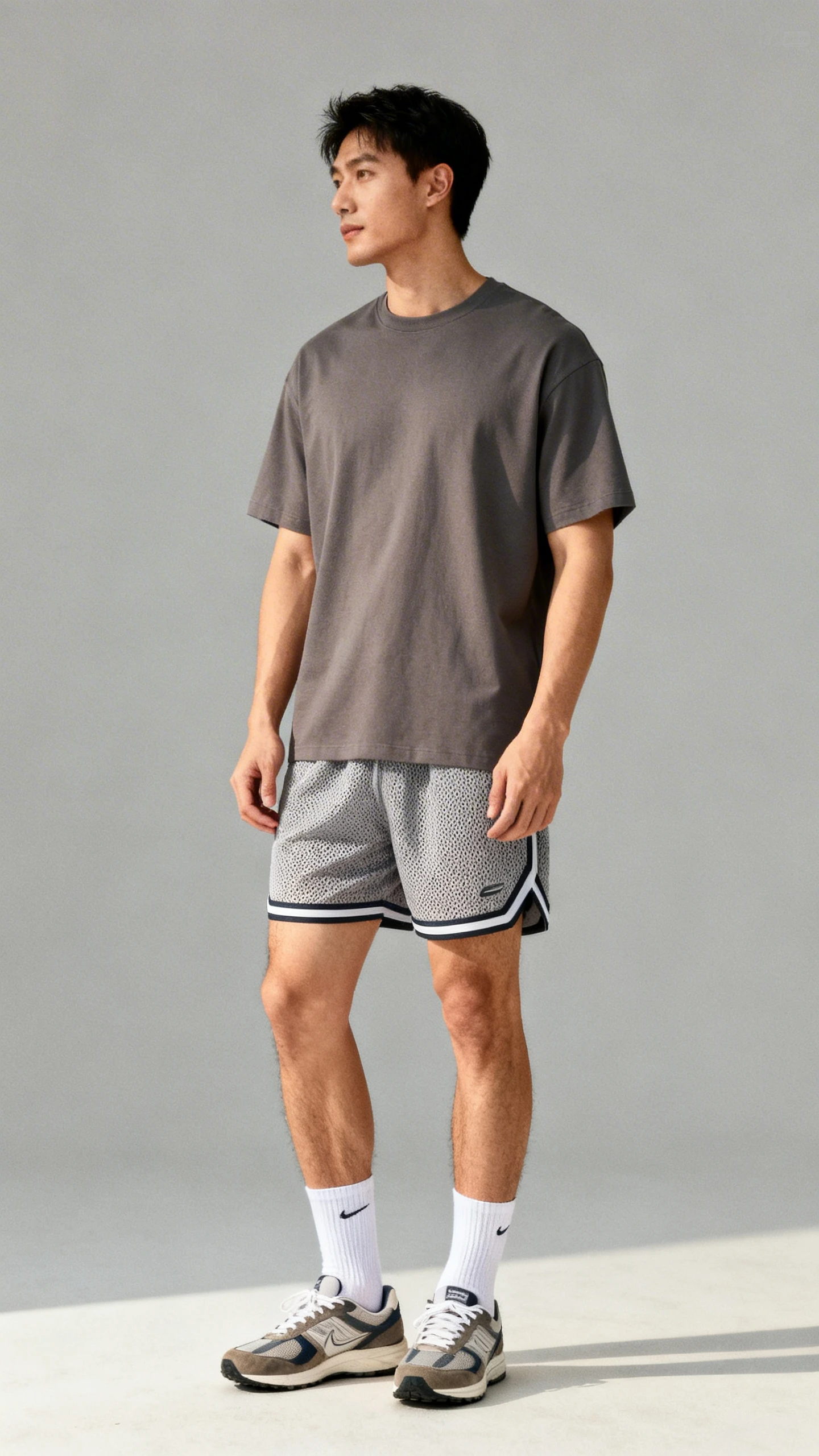 Editorial studio image of a man in athletic-casual mesh shorts with a relaxed heavyweight tee, crew socks, and retro runners, gray background, soft studio lighting, easy stance, clean composition, high quality.