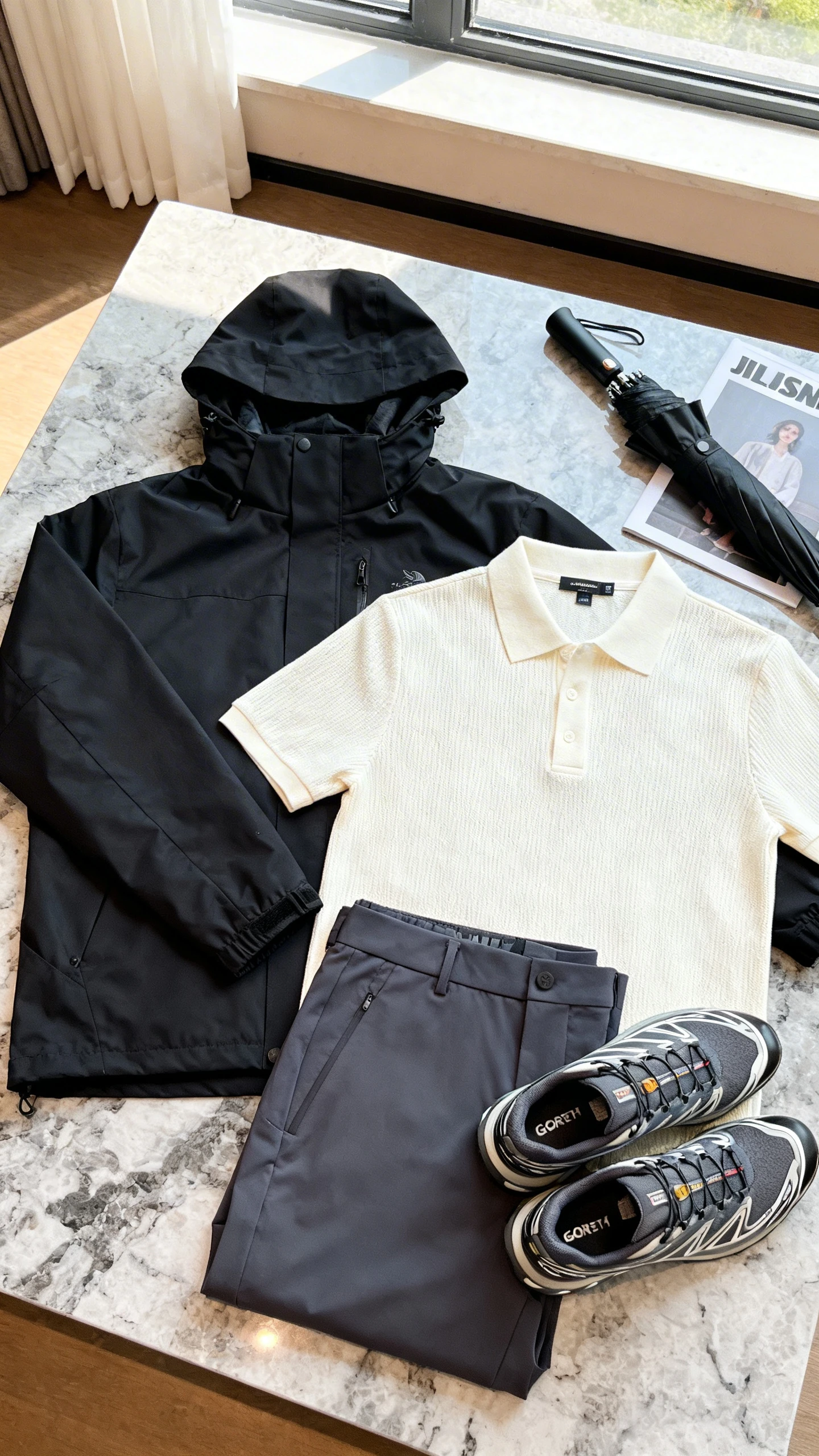 Flat lay overhead of a black water-resistant tech shell, cream short-sleeve knit polo, tailored performance trousers in charcoal, sleek Gore-Tex trainers, and a compact umbrella, set on a marble countertop with a magazine as prop, bright natural window light, no person visible, organized composition, iPhone photo aesthetic.